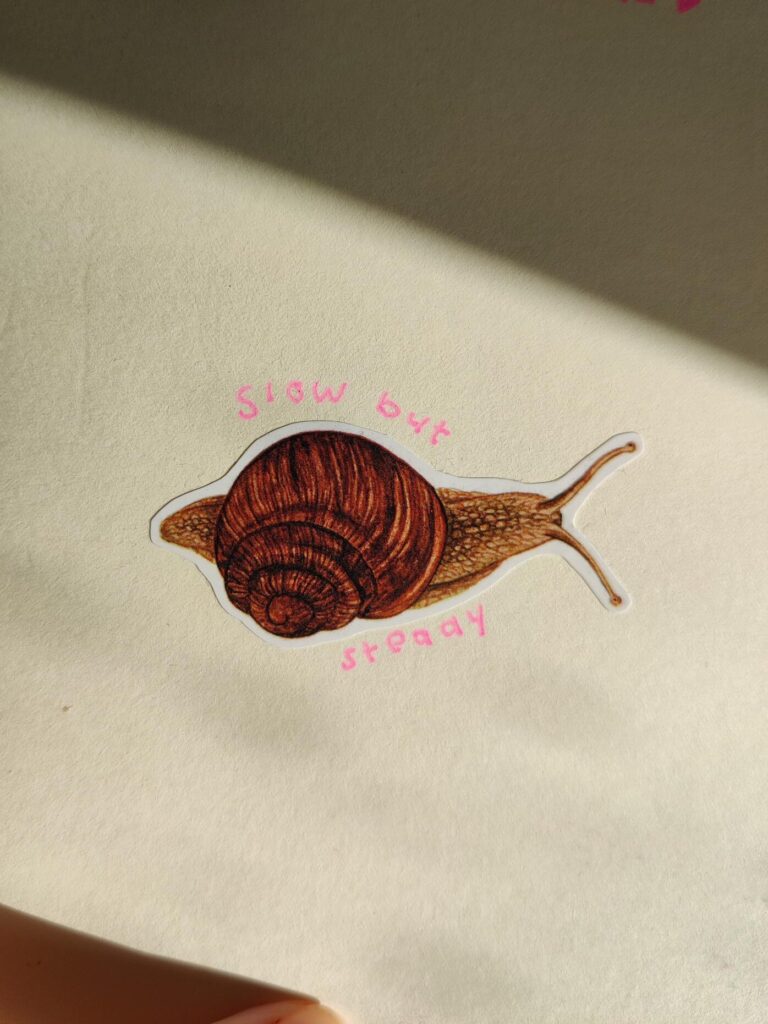 Sticker of a snail with the text 'slow but steady' written around it.