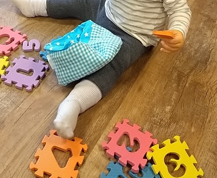 Baby legs surrounded by foam puzzle pieces.